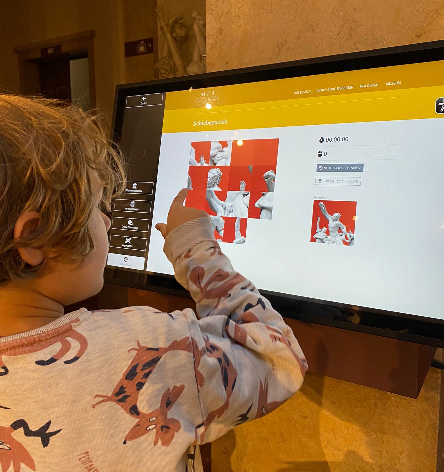 Ein Kind probiert ein Touchbildschirm im Museum aus, auf dem die digitale Datenbank zu sehen ist.