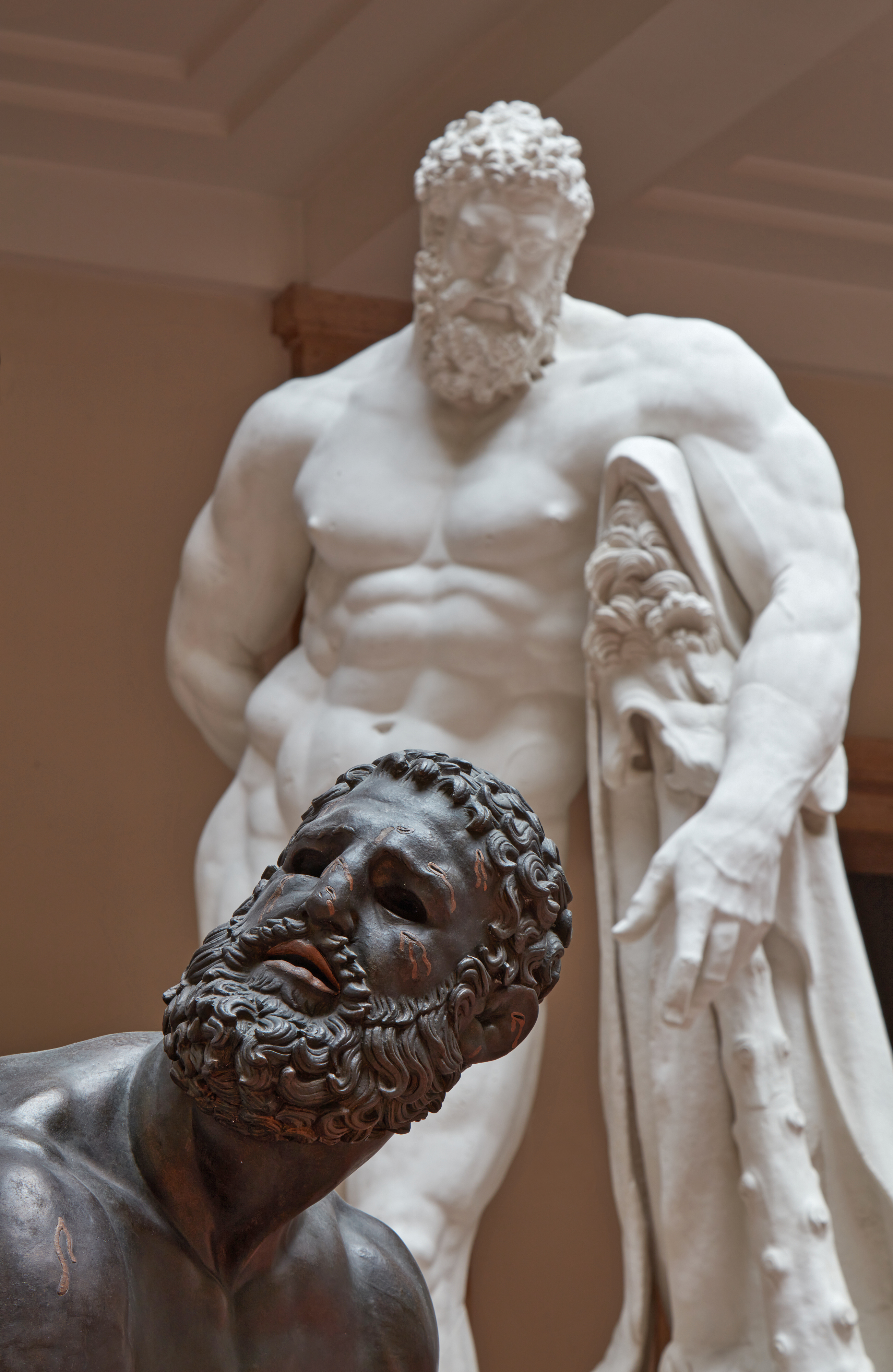 Kopf eines bärtigen Mannes vor einer nackten Skulptur eines muskulösen, bärtigen Mannes
